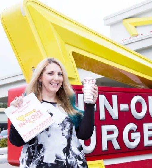 kc with a burger and drink standing in front of the in n out sign