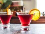 two pomegranate martinis with orange slices