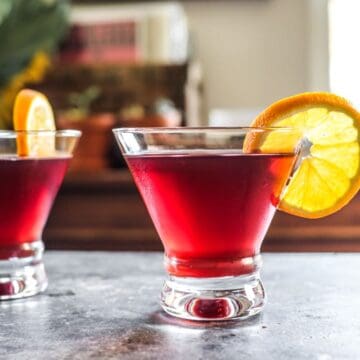 two pomegranate martinis with orange slices