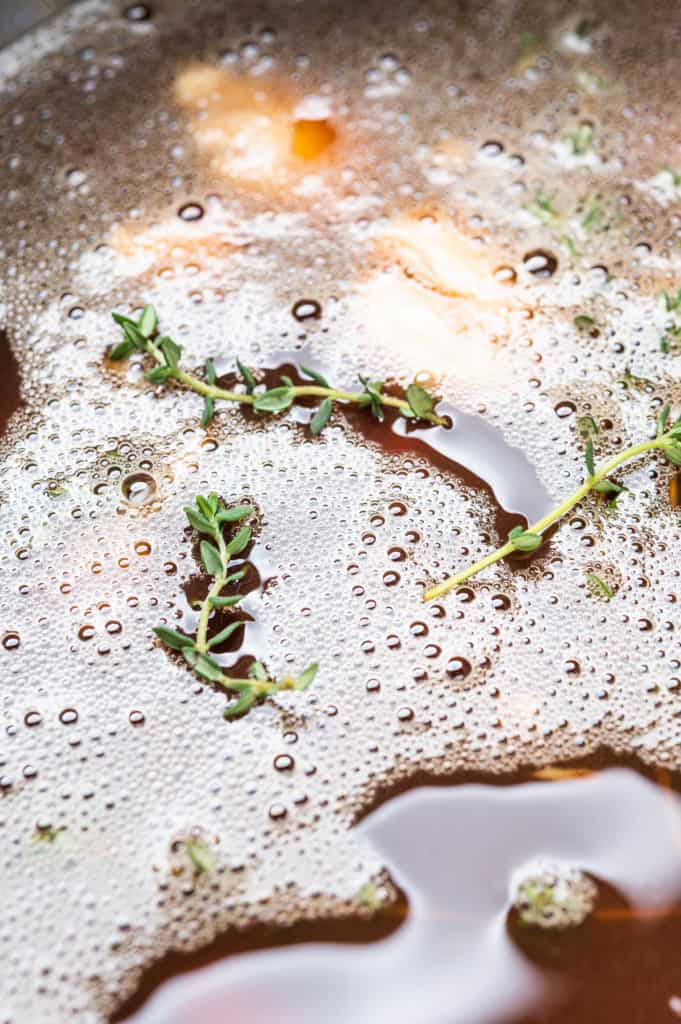 a closeup of the tea brine with fresh thyme sprigs floating on the surface