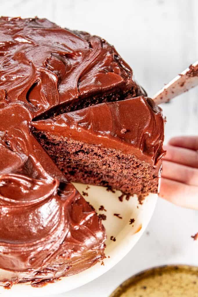 Removing a slice of Devil's Food Cake from a whole chocolate cake with chocolate frosting