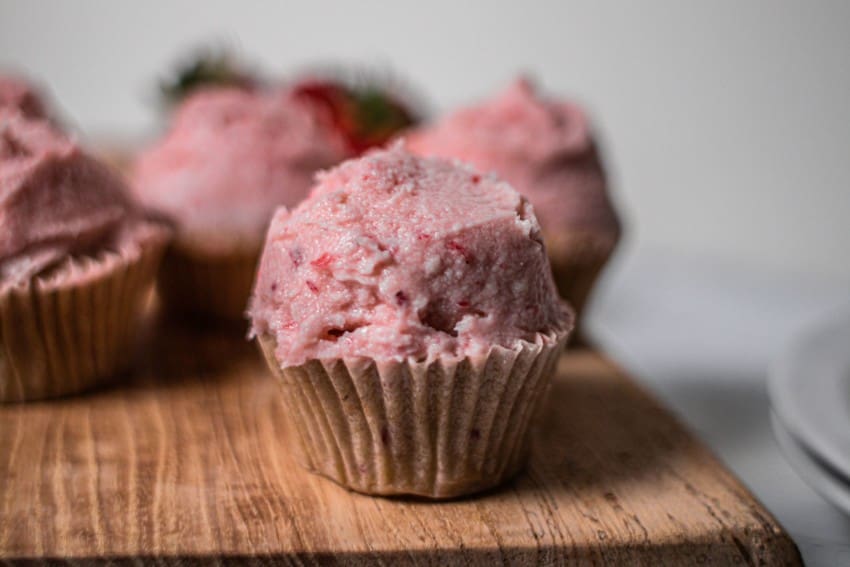 pink strawberry cupcakes on top of a wooden board