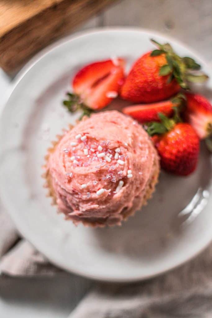 one strawberry cupcake served on a white plate with a side of strawberries