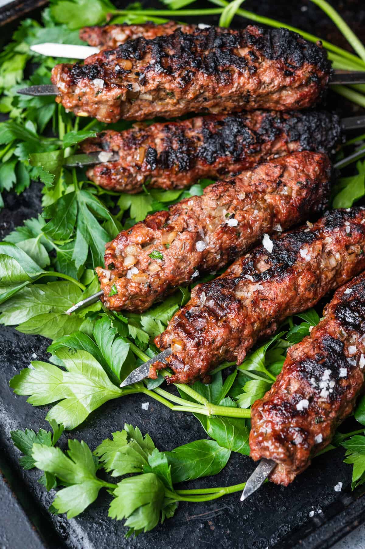 Charred lamb mince on metal skewers sat on a bed of coriander leaves.