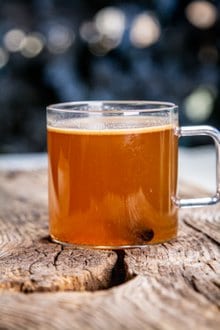 A clear mug full of hot buttered rum on a wooden board. 