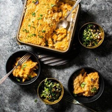 An overhead shot of a pan of baked mac & cheese, surrounded by a few bowls of mac & cheese & salad