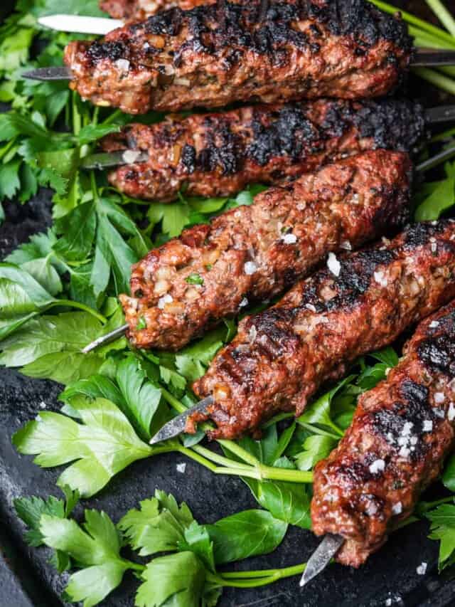 A stack of Lula Kebabs on a bed of parsley on a black board