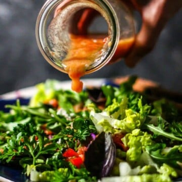 hand pouring a jar of tomato vinaigrette over a mixed greens salad