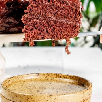 A knife holding a slice of chocolate devils food cake hovering over a yellow plate