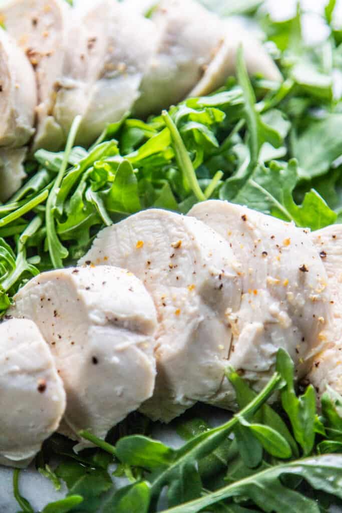 sliced poached chicken breast on a bed of arugula