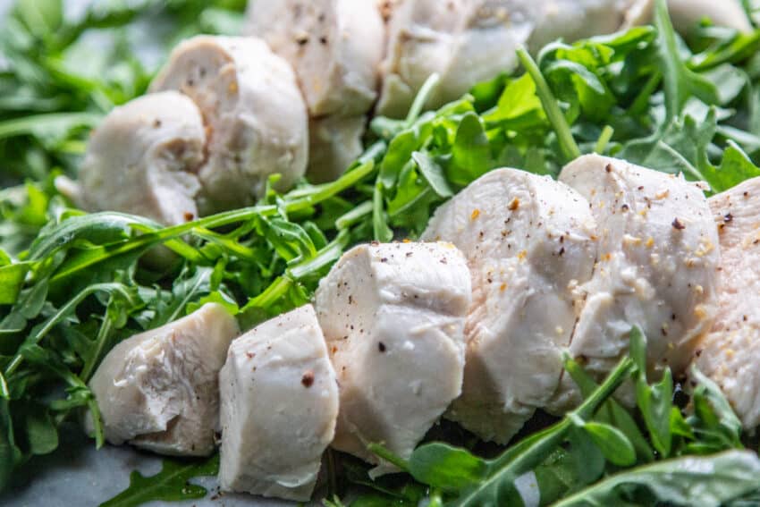 sliced poached chicken breast on a bed of arugula