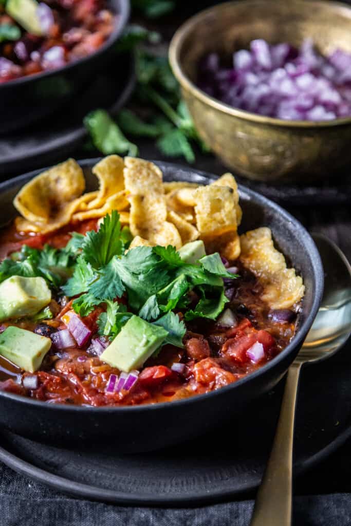 two bowls of homemade chili surrounded by bowls of chili toppings