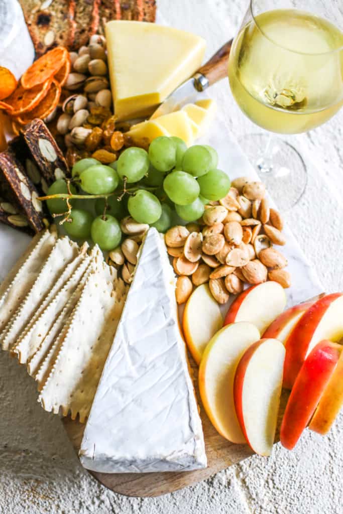 a graze board with brie, cheddar, fruit, nuts, crackers and wine