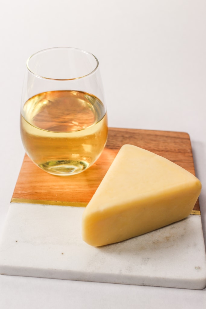 cheese on a cutting board with a glass of wine