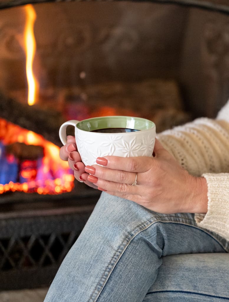 woman sitting in front of a fireplace with a cup of coffee