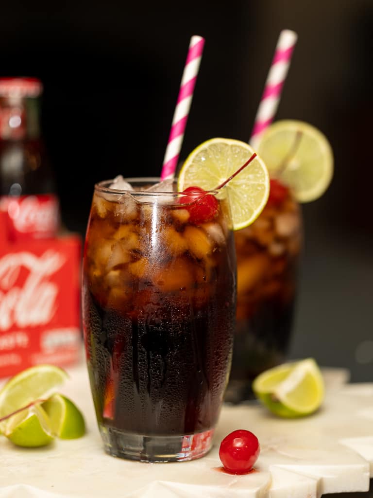 two glasses of coke with cherries, lime and a straw