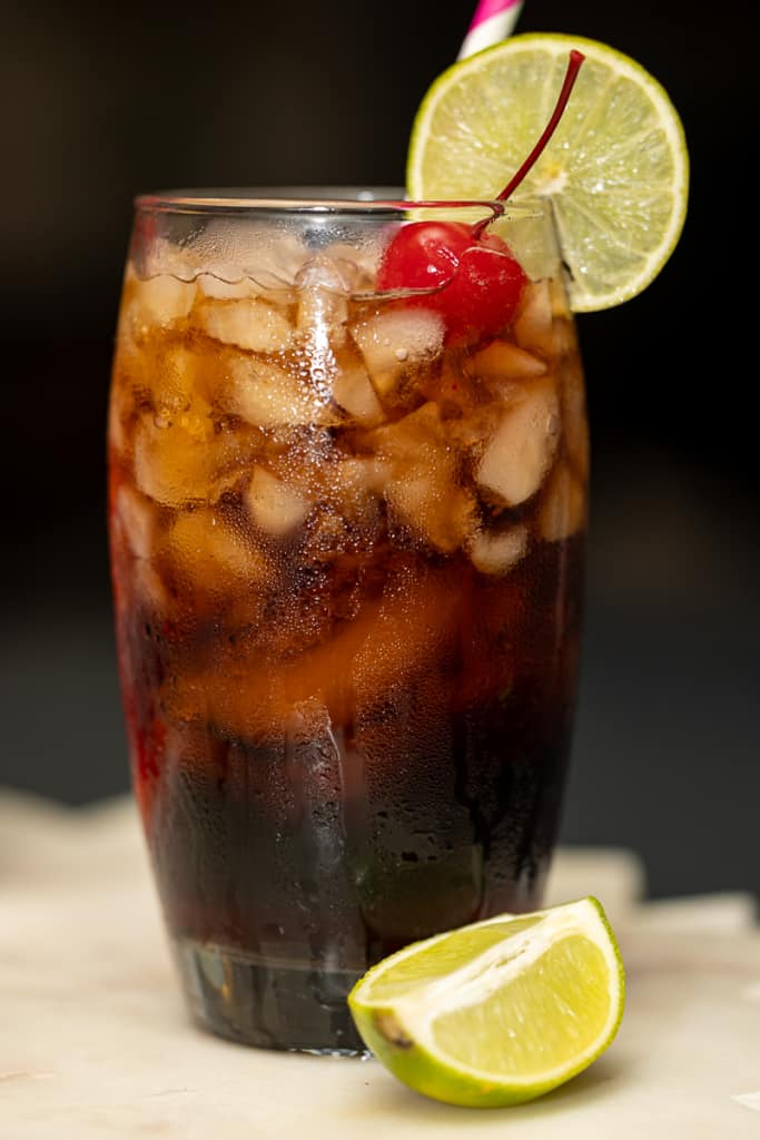 close up of a glass of soda with a cherry and lime