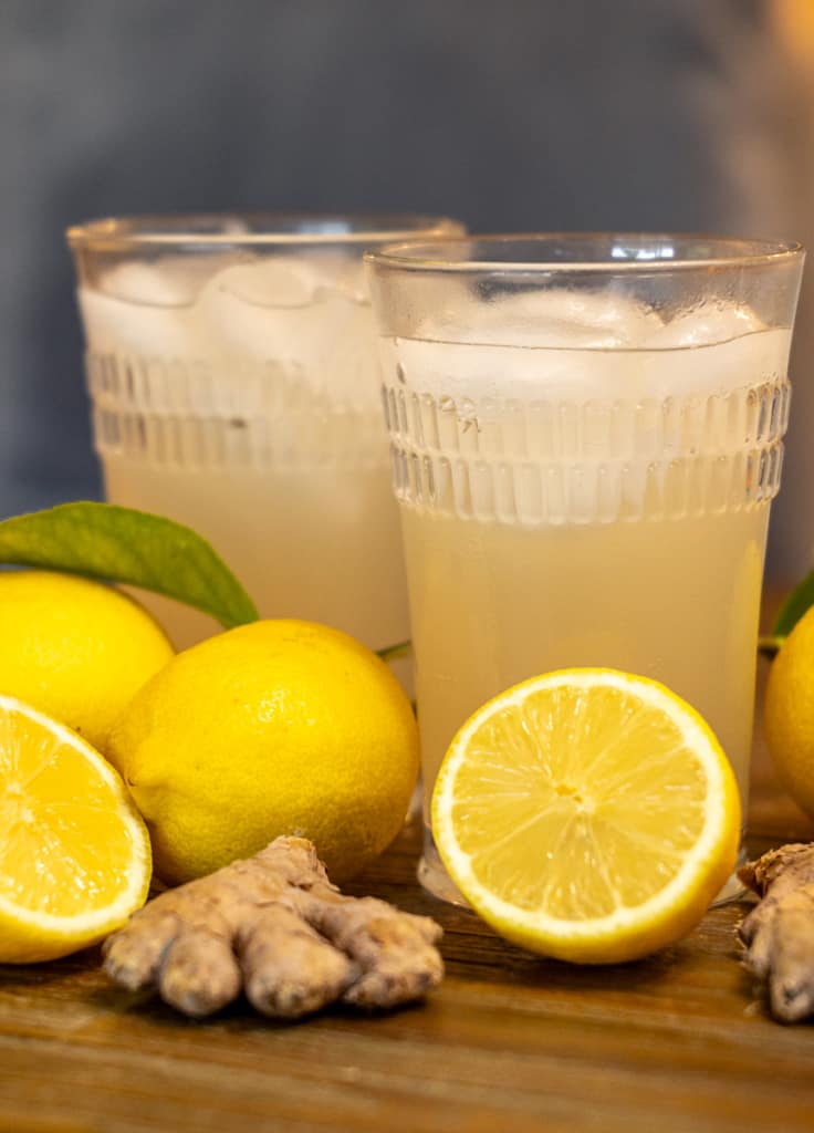 two glasses of ginger beer surrounded by lemons and ginger