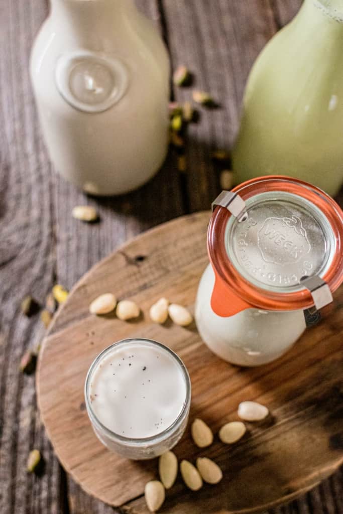 a glass of almond milk on a board with almonds and a jug of milk