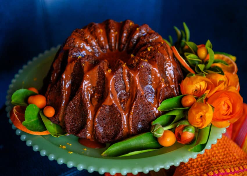 Chocolate Orange Cake with Chocolate Glaze on a cake stand with flowers and kumquats