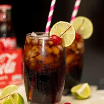 two glasses of coke with cherries, lime and a straw