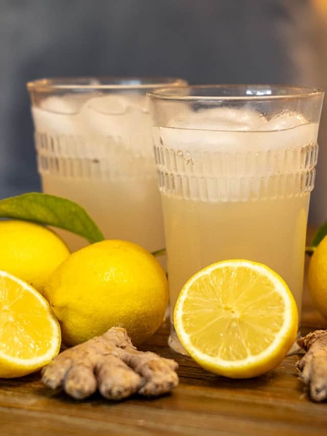 two glasses of ginger beer surrounded by lemons and ginger
