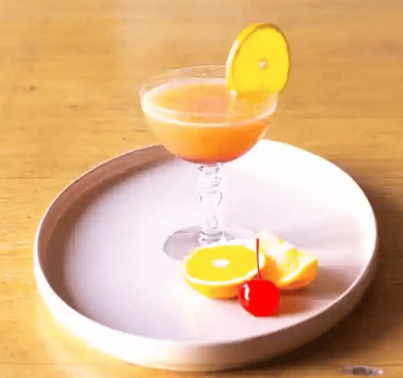 a glass with a tequila sunrise cocktail and fruit garnish from Hola Jalapeno