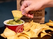 hand scooping guacamole onto chipotle chips