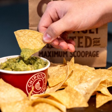 hand scooping guacamole onto chipotle chips