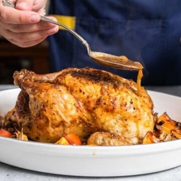 A whole roastd chicken with sauce being spooned over the top.