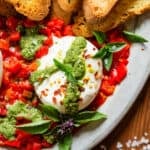 burrata appetizer on platter with red peppers, basil pesto and fresh basil
