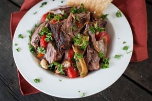 shredded lamb shoulder in a serving bowl with peppers and garlic - lamb shoulder cooked in the oven