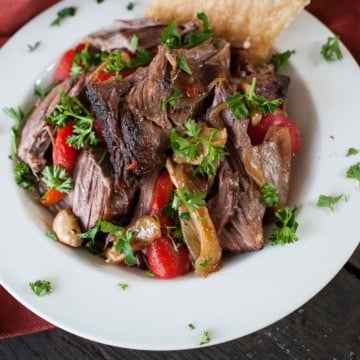 shredded lamb shoulder in a serving bowl with peppers and garlic - lamb shoulder cooked in the oven
